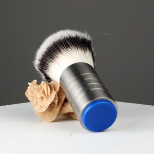 Op de afbeelding: Een zilveren scheerkwast met een blauwe basis en een wit en zwart borstelhoofd.