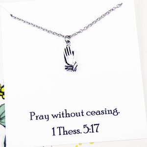 May include: A silver necklace with a praying hands pendant. The necklace comes on a card with the text "Pray without ceasing. 1 Thess. 5:17"