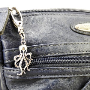May include: A silver octopus charm attached to a silver key chain. The charm is hanging from a blue zippered bag.