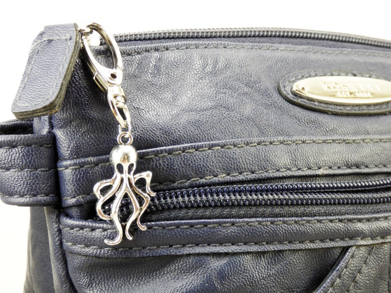 May include: A silver octopus charm attached to a silver key chain. The charm is hanging from a blue zippered bag.
