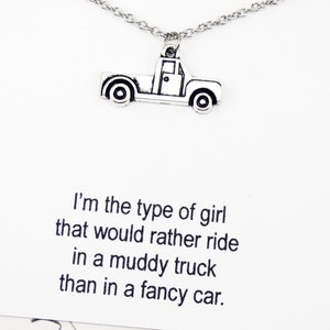 Op de afbeelding: Een zilveren ketting met een truckbedel en een kaart met de tekst "Ik ben het type meisje dat liever in een modderige truck rijdt dan in een chique auto."