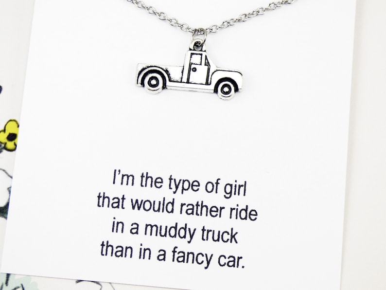 Op de afbeelding: Een zilveren ketting met een truckbedel en een kaart met de tekst "Ik ben het type meisje dat liever in een modderige truck rijdt dan in een chique auto."