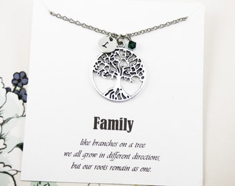 May include: A silver necklace with a tree of life pendant and a small green crystal charm. The pendant has a small silver disc with the letter "L" on it. The necklace comes with a card that reads "Family like branches on a tree we all grow in different directions, but our roots remain as one."