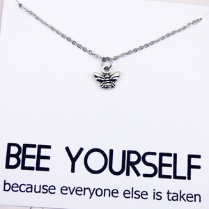 May include: A silver necklace with a small bee charm. The necklace has a white card attached to it with the text "BEE YOURSELF because everyone else is taken."