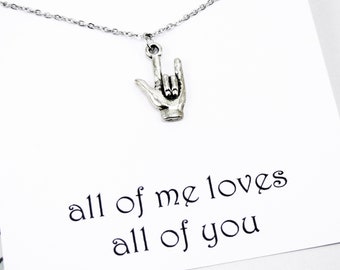 May include: Silver-toned necklace featuring a pendant in the shape of a hand making the "I love you" sign in American Sign Language. The pendant hangs from a delicate chain. The card behind the necklace reads "all of me loves all of you."