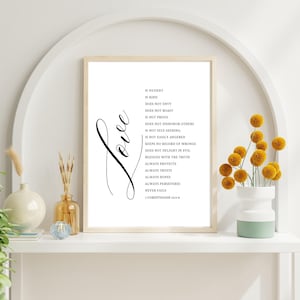 May include: A framed print with the word "Love" in cursive script and a list of virtues. The text is in black on a white background. The frame is light-colored, and the print is displayed on a white shelf with decorative vases and flowers.