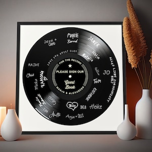 May include: A black vinyl record with white text around the edge, including names such as "Ramona", "Marie", and "Janek". The centre of the record has a white star and the text "For the Record Please Sign Our Guest Book Manja & Alexander".