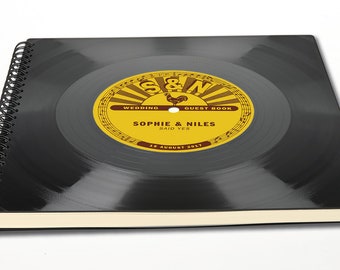 May include: Black spiral bound guest book with a vinyl record design. The label on the record says "S&N Wedding Guest Book, Sophie & Niles Said Yes, 18 August 2017."