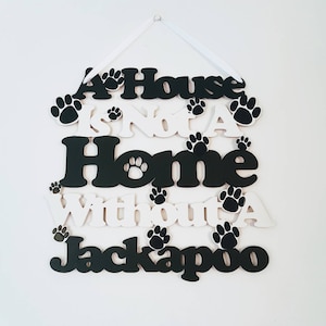 May include: A white wooden sign with black lettering that reads "A House Is Not A Home Without A Jackapoo". The sign has paw prints around the lettering.