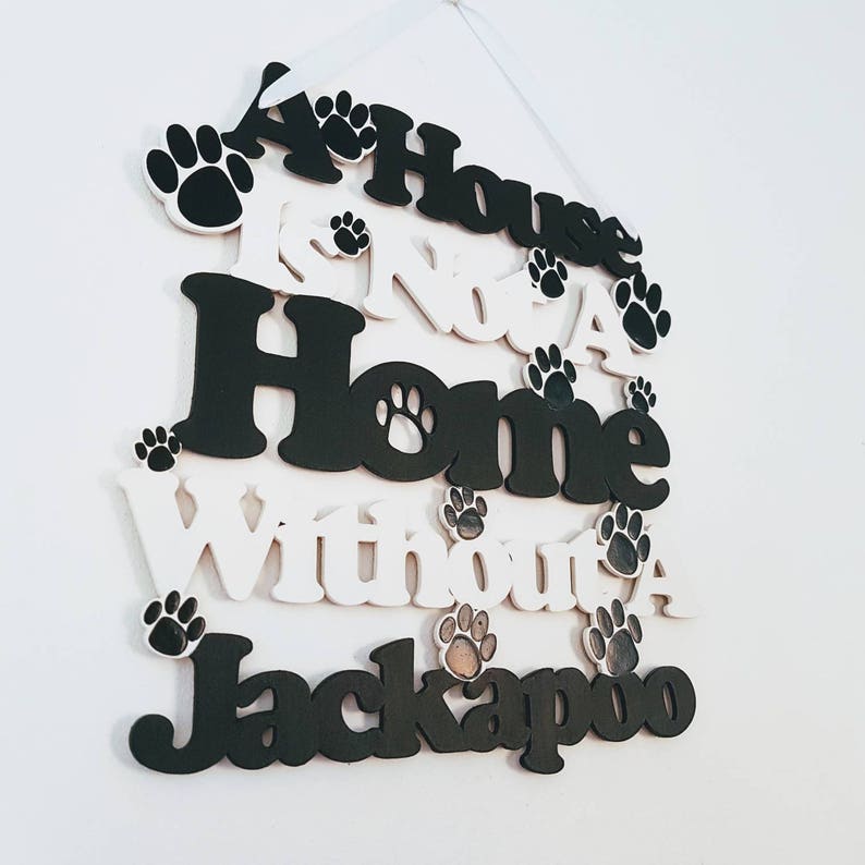 Op de afbeelding: Een zwart-wit houten bord met de tekst "A House Is Not A Home Without A Jackapoo". Het bord is versierd met poot afdrukken.