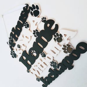 Op de afbeelding: Een wit houten bord met de woorden "A House Is Not A Home Without A Jackapoo" in zwarte letters. Het bord is versierd met zwarte hondenpootjes.