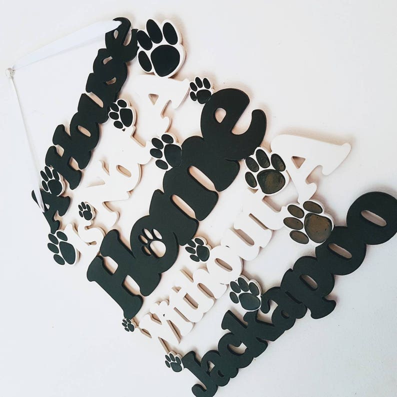 Op de afbeelding: Een wit houten bord met de woorden "A House Is Not A Home Without A Jackapoo" in zwarte letters. Het bord is versierd met zwarte hondenpootjes.