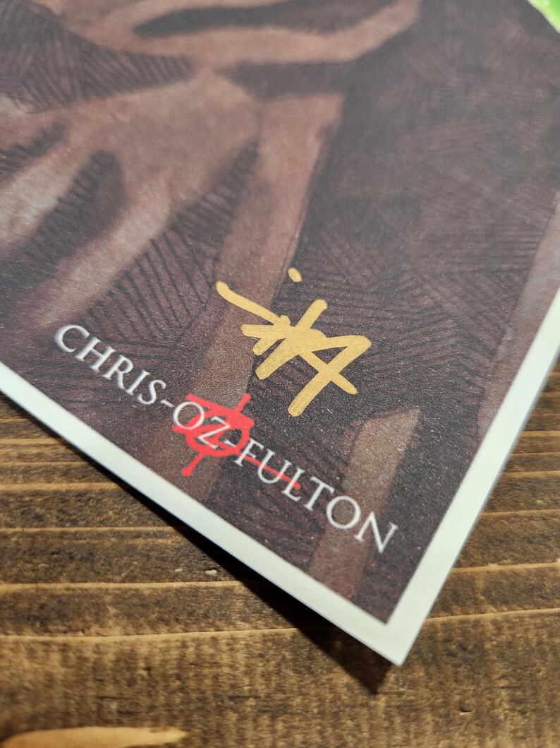 May include: A close-up of a signature by Chris-Oz Fulton, written in gold ink on a white background. The signature is on a brown textured surface.