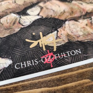 May include: A black and white drawing of hands with a gold signature that reads "CHRIS-OZ FULTON" in a stylised font.