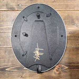 Peut inclure: Un cadre photo ovale noir avec un logo dor&eacute; "Stussy" au dos. Le cadre est dot&eacute; d'un crochet de suspension au dos.