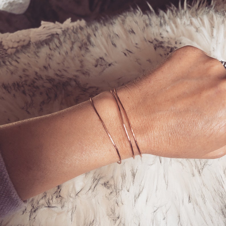 May include: Three thin gold bangles stacked on a wrist. The bangles are made of a smooth, shiny metal.