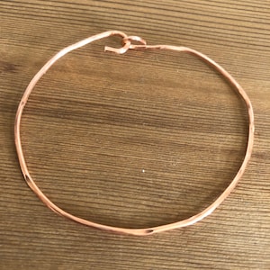 May include: A simple, hammered copper bangle bracelet with a smooth, rounded finish.