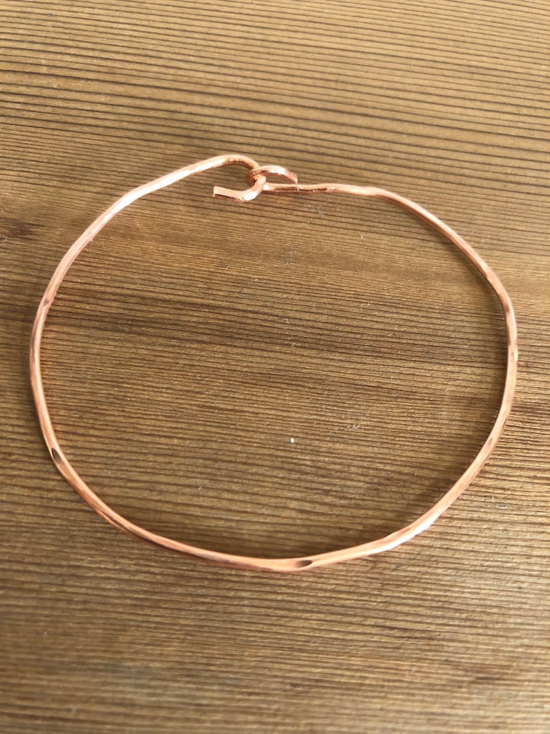 May include: A simple, hammered copper bangle bracelet with a smooth, rounded finish.
