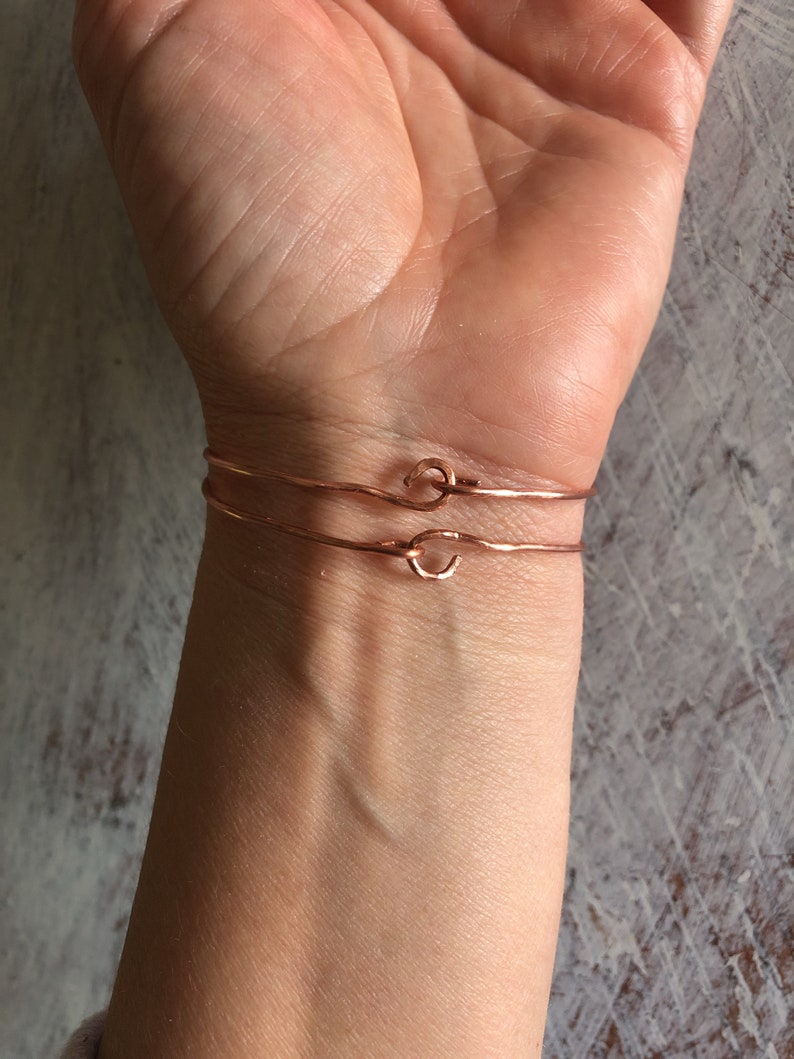 May include: Two thin rose gold bracelets with a knot detail on the wrist of a person.