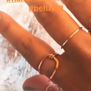 May include: A close-up of a hand wearing three copper rings. The rings are simple and delicate, with a hammered finish. The hand is resting on a light wood surface. The image includes the hashtags #handmade #copper #beltring.