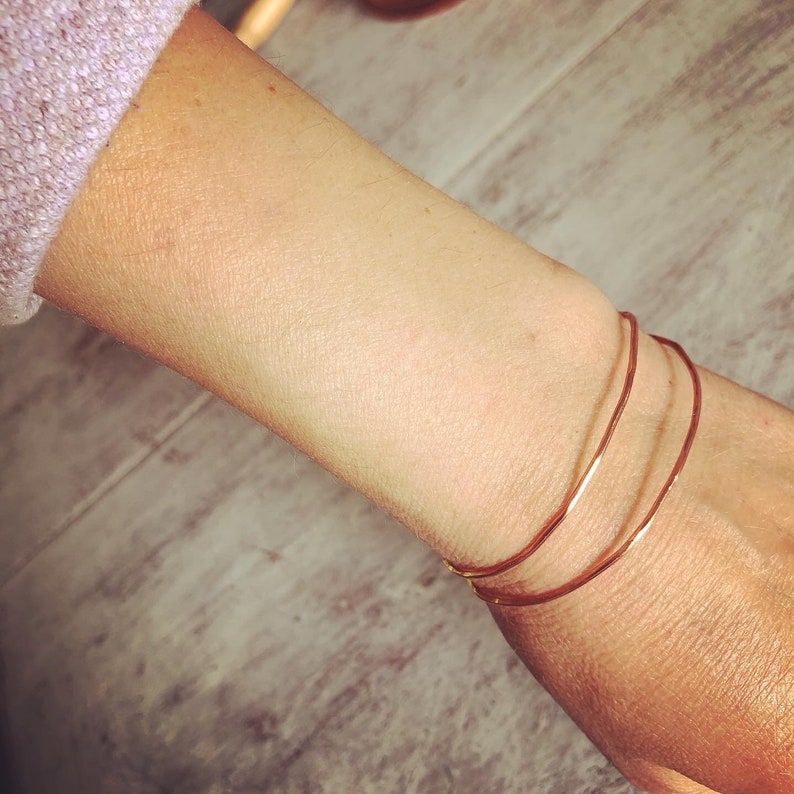 May include: Three gold bangle bracelets stacked on a person's wrist.