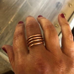May include: A copper ring with five bands stacked on top of each other. The ring is worn on a person's finger.