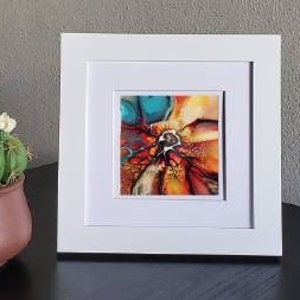 May include: Abstract art painting in a white frame. The painting features a swirling mix of orange, yellow, red, and blue colors.
