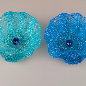 May include: Two blue glass seashell-shaped bowls with a blue gem in the center of each bowl.