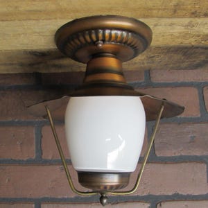 May include: A vintage ceiling light fixture with a white glass shade and a brass finish. The light has a decorative design on the top and bottom.