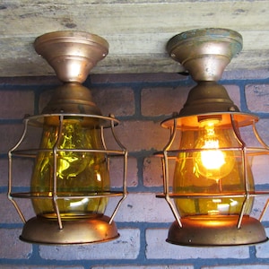 May include: Two antique copper ceiling light fixtures with caged amber glass shades. The lights are on and the bulbs are glowing.