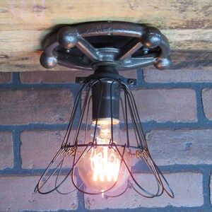 May include: A black metal ceiling light fixture with a cage-style lampshade and a vintage-style wheel-shaped base. The light is on and illuminating the room.