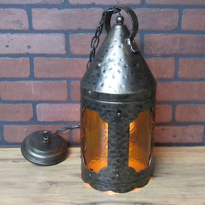 May include: A hammered metal pendant light fixture with a amber glass shade. The light is hanging from a chain and has a decorative metal cap.