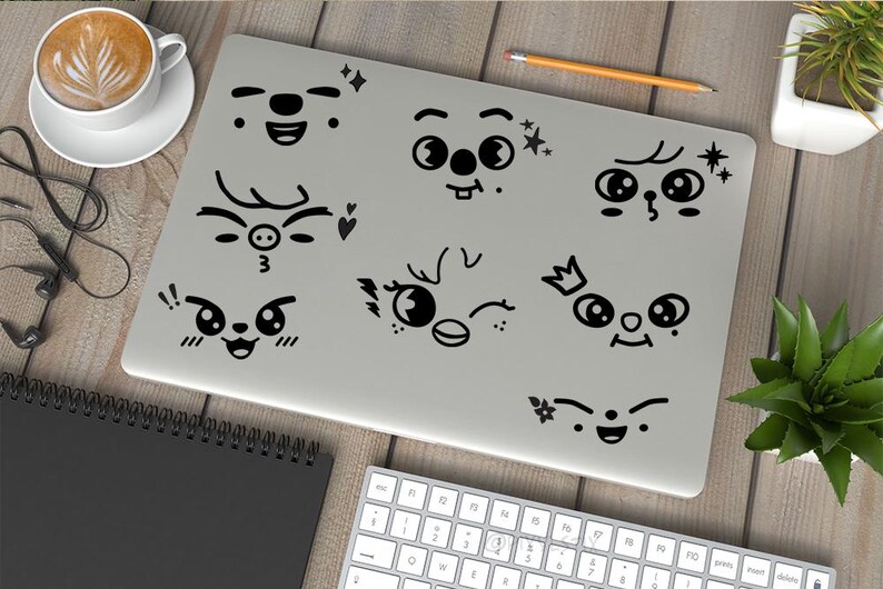 May include: A silver laptop with black cartoon faces with different expressions on the lid. The faces include a deer, a pig, a bird, a cat, and a few other faces with different expressions.