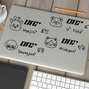 May include: A white laptop with black stickers featuring cartoon animals and the text "ONT" with names and Korean characters written below each sticker.