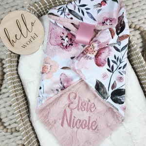 May include: A pink and white floral print baby blanket with a soft pink minky backing. The blanket is personalized with the name "Elsie Nicole" embroidered in pink thread.