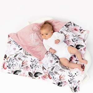 May include: A pink and white baby blanket with a floral pattern. The blanket has a soft, plush side and a cotton side. The blanket is personalized with the name "Lila Rue" embroidered on the pink side.