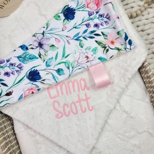 May include: White baby blanket with a floral print on one side and the name "Emma Scott" embroidered on the other side.