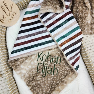 May include: A brown and white striped baby blanket with a soft, fuzzy brown side. The blanket is personalised with the names "Kohnen Elijah" embroidered in green.