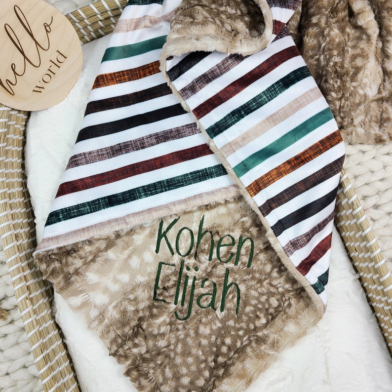 May include: A brown and white striped baby blanket with a soft, fuzzy brown side. The blanket is personalised with the names "Kohnen Elijah" embroidered in green.