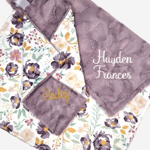 Puede incluir: Una manta de beb&eacute; floral de color morado y blanco con los nombres "Hayden Frances" y "Cailey" bordados en hilo dorado.