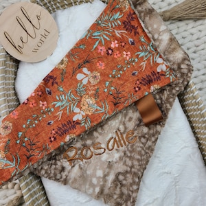 May include: A brown and white faux fur baby blanket with an orange floral fabric on top. The blanket has the name "Rosalie" embroidered on it.