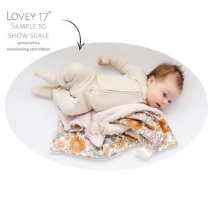 May include: A baby lying on a white background with a floral patterned blanket. The blanket is 17 inches and comes with a coordinating satin ribbon. "Lovey 17" is written on the image.