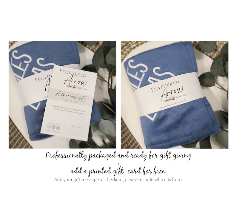 Puede incluir: Una manta azul y blanca con la palabra "bless" bordada. La manta est&aacute; doblada y empaquetada con una tarjeta blanca que dice "Feathered Arrow" y "A special gift".