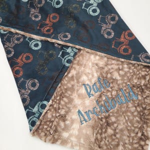 May include: A blue and brown baby blanket with a tractor pattern on one side and a soft, brown faux fur on the other side. The blanket is personalised with the name "Rafe Archibald" embroidered in blue thread.