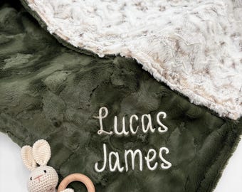 Puede incluir: Una manta suave y afelpada con un lado verde oliva oscuro y otro de piel sintética color crema. El nombre Lucas James está bordado en blanco sobre el lado verde. Incluye un pequeño conejo de ganchillo beige unido a un anillo de madera.