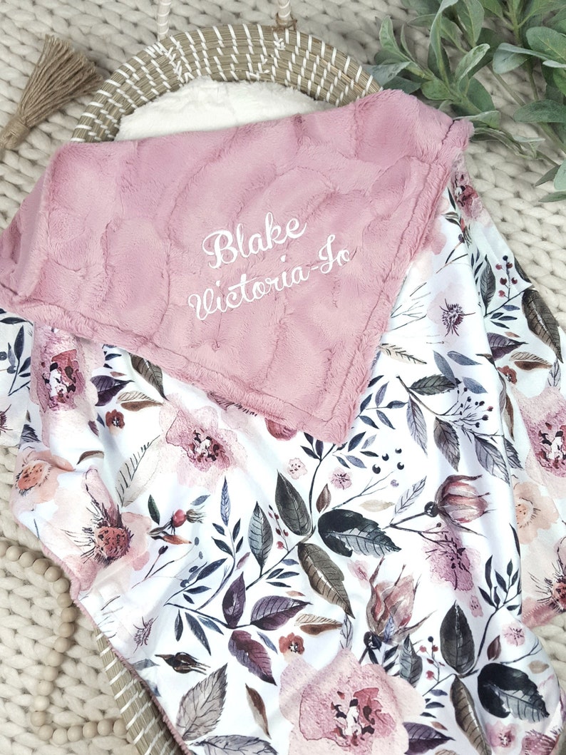 May include: A pink and white floral baby blanket with a soft, plush side. The blanket is personalized with the names "Blake Victoria-Jo" embroidered in white.