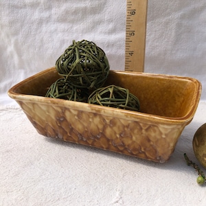 以下が含まれることがあります： 茶色とベージュの釉薬がかかった長方形のセラミックプランター。プランターには、緑色の編まれたボールが3つ入っています。