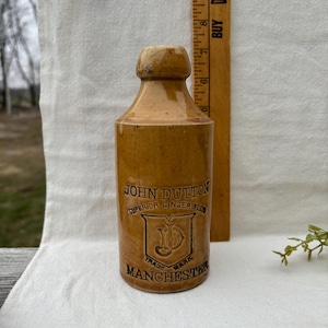 May include: A white ceramic mug with a black handle and the text "But First, Coffee" in a bold, black font. The mug is set against a blurred background, suggesting a cozy setting.
