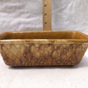 May include: A rectangular ceramic planter with a glossy brown glaze and a textured diamond pattern on the exterior. A wooden ruler is positioned vertically behind the planter, showing a height measurement of approximately 6.5 cm.
