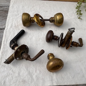 May include: An assortment of vintage door hardware, including brass and bronze doorknobs and handles. The collection features various shapes and styles, showcasing aged patina and classic designs. Ideal for restoration projects or adding a touch of antique charm.
